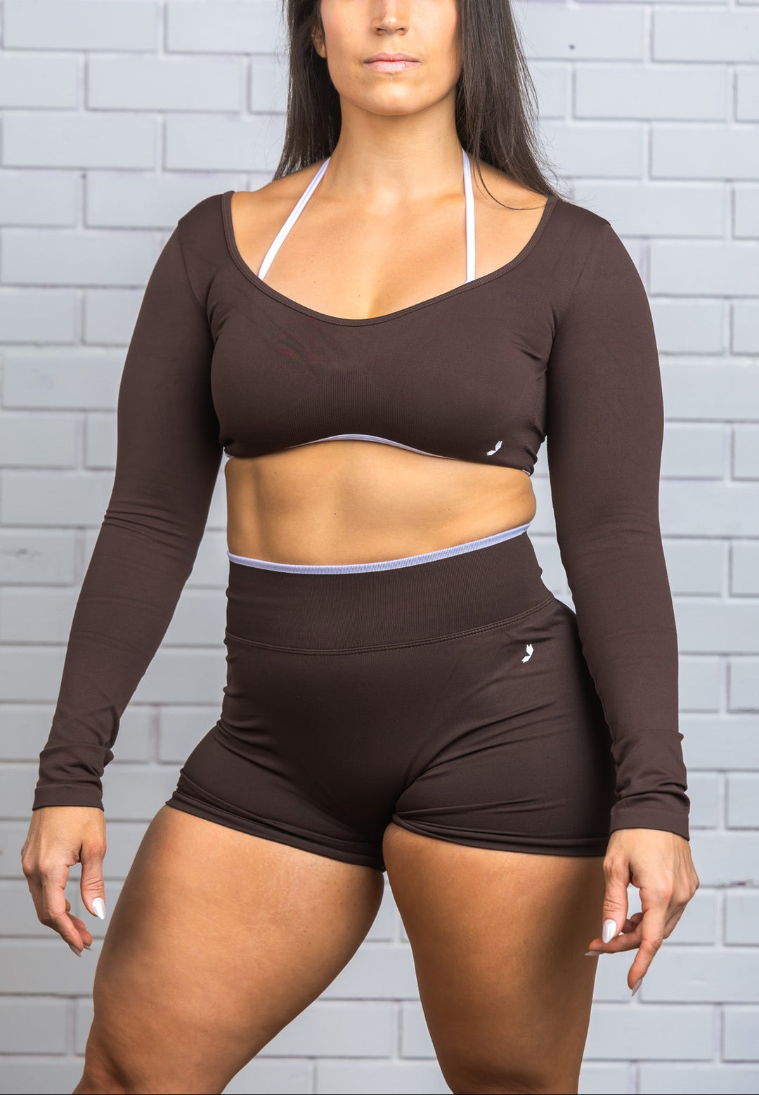 Woman wearing a brown athletic outfit against a gray brick wall.
