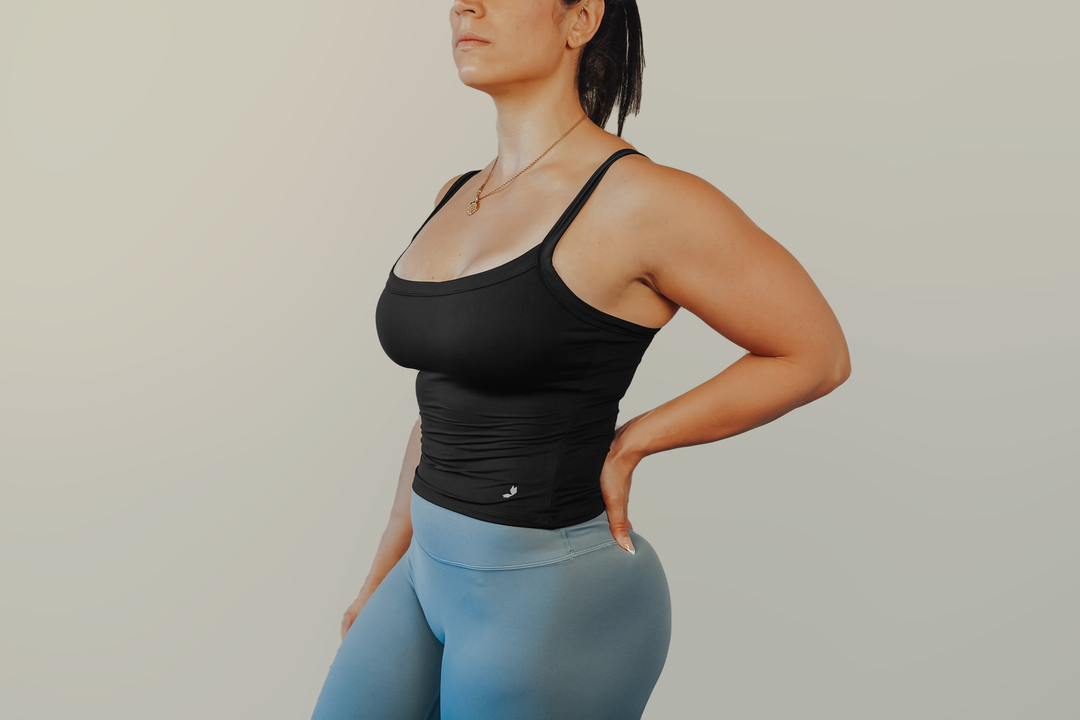 Woman wearing a black athletic tank top and blue leggings against a plain background
