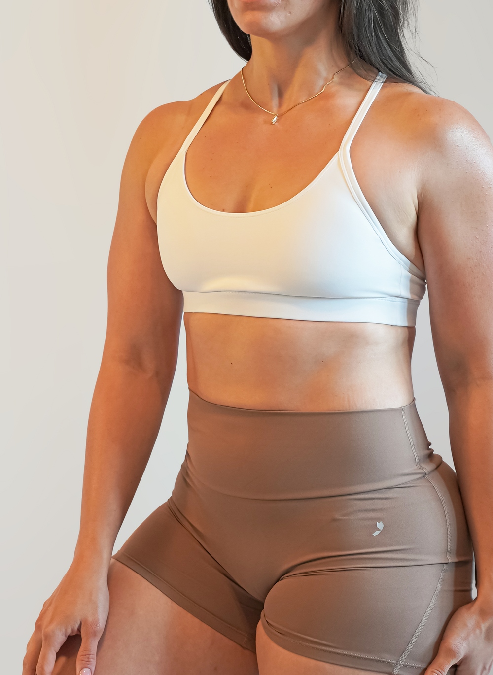 Woman wearing a white sports bra and brown shorts on a plain background
