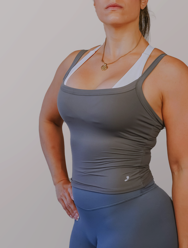 Woman wearing a gray tank top and blue leggings against a plain background