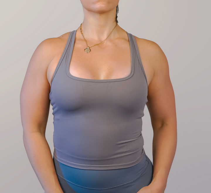Woman wearing a gray tank top and blue leggings against a plain background