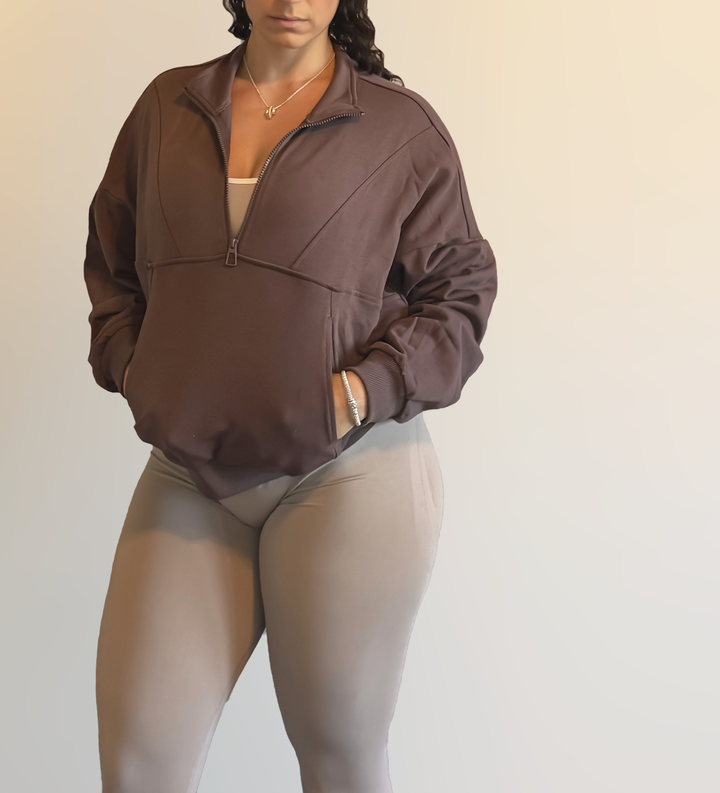 Person wearing a brown jacket and beige leggings against a plain background