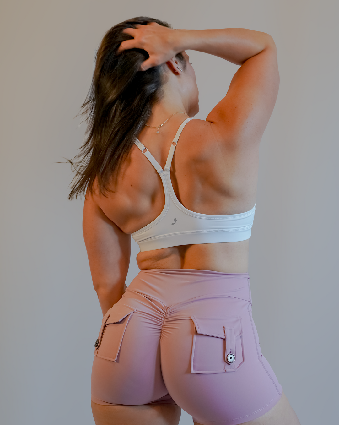 Woman in a white sports bra and pink shorts stretching against a plain background