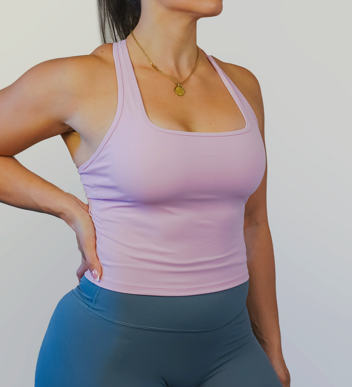 Woman wearing a light pink tank top and blue grey leggings against a plain background