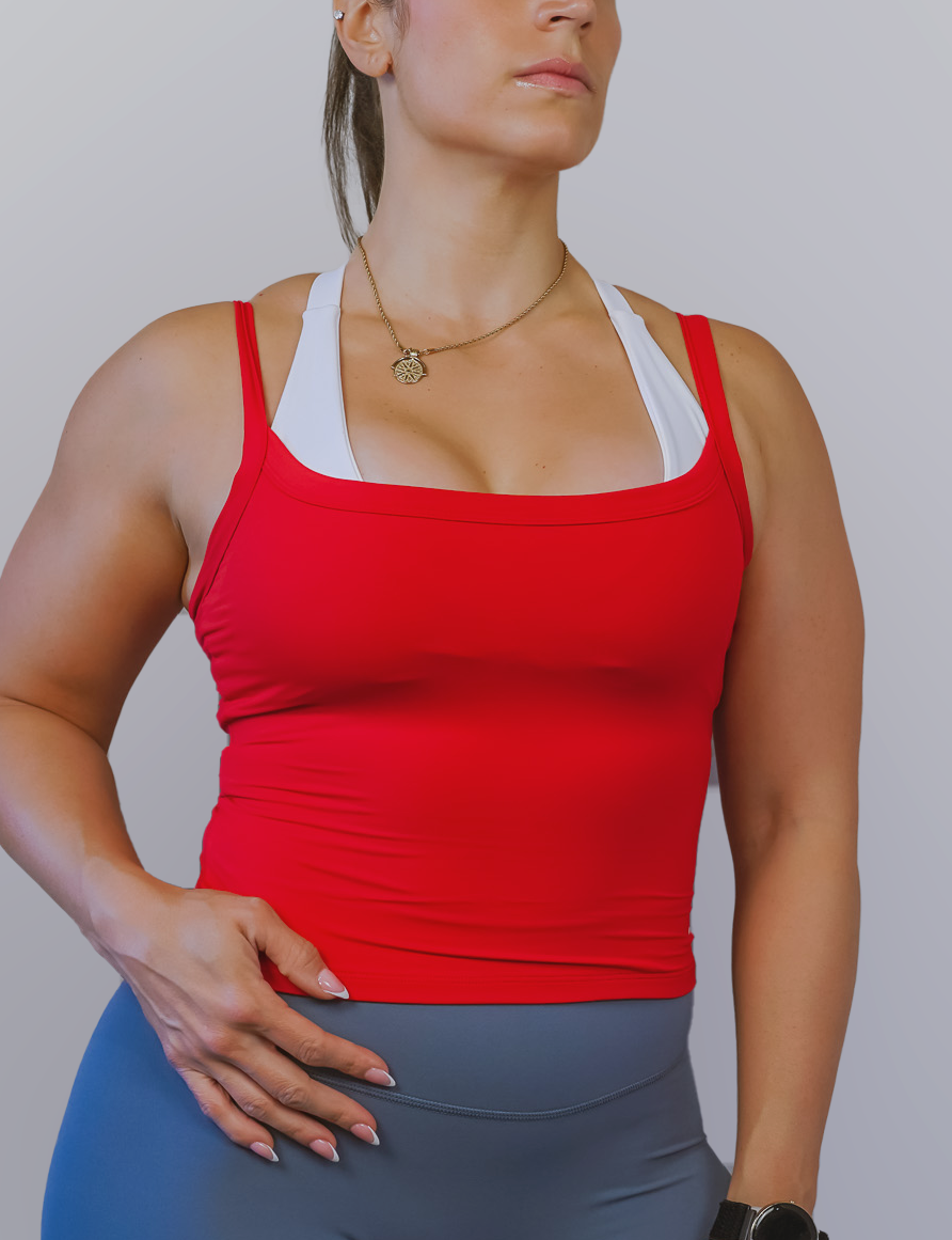 Woman wearing a red tank top and gray leggings against a plain background
