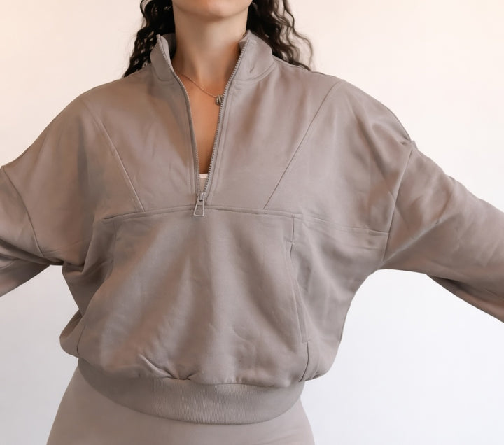 Person wearing a beige zip-up sweatshirt on a plain background