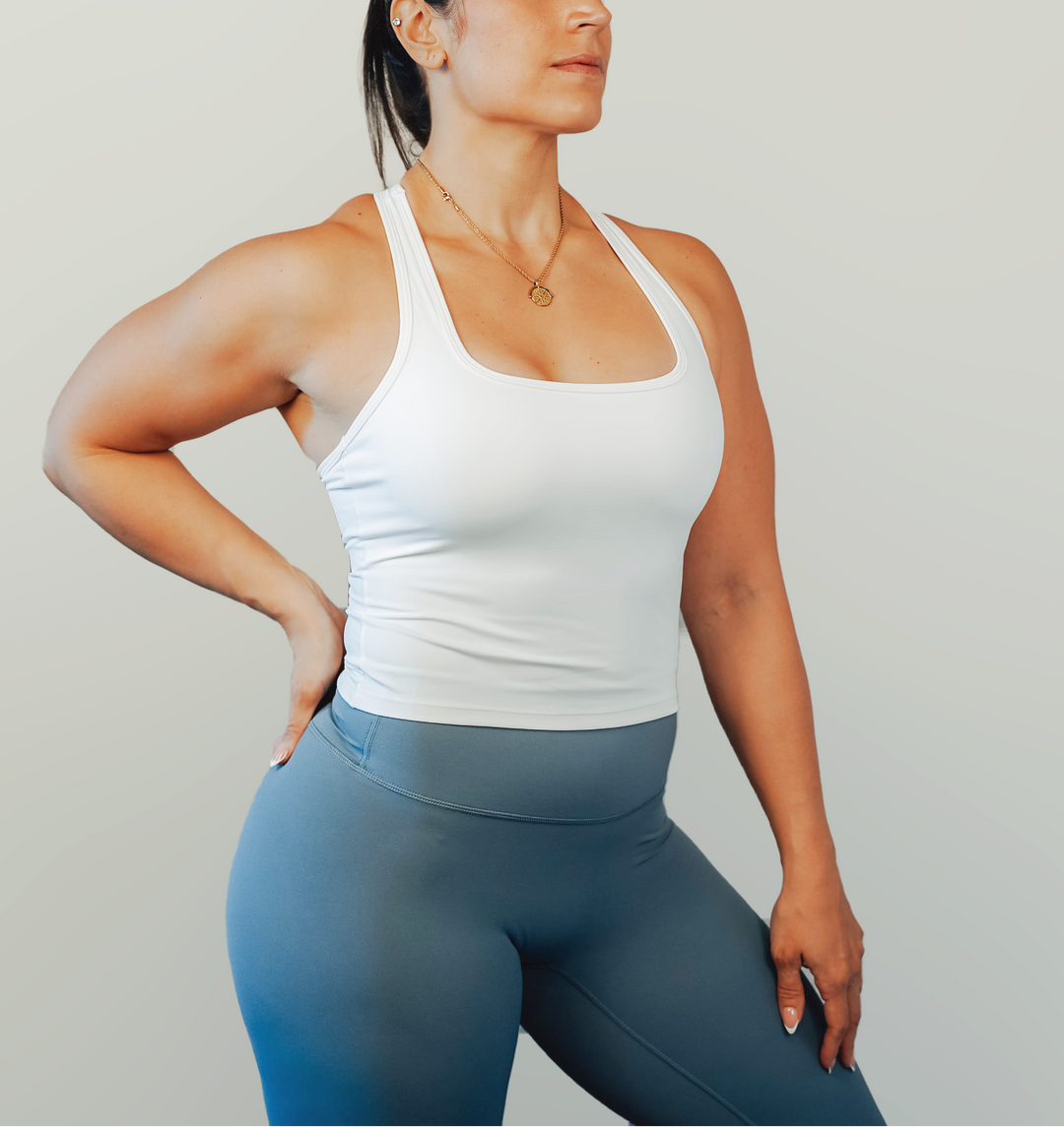 Woman wearing a white tank top and blue leggings against a plain background